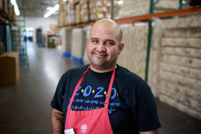 A thrift store worker wearing a red apron smiles as he helps store donations