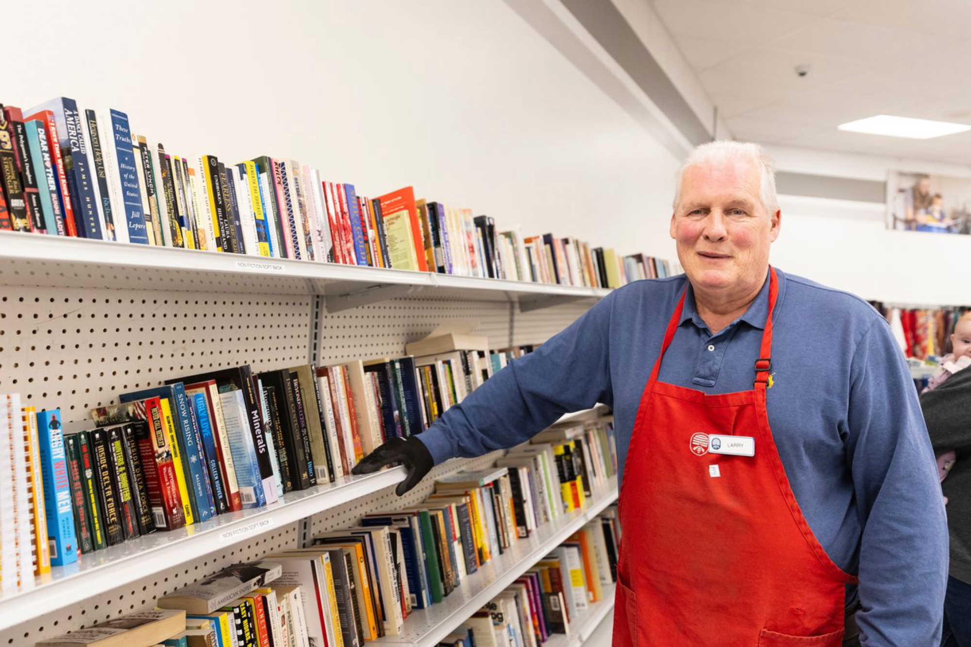 thrift store employee smiles as he stands in the book section at Deseret Industries