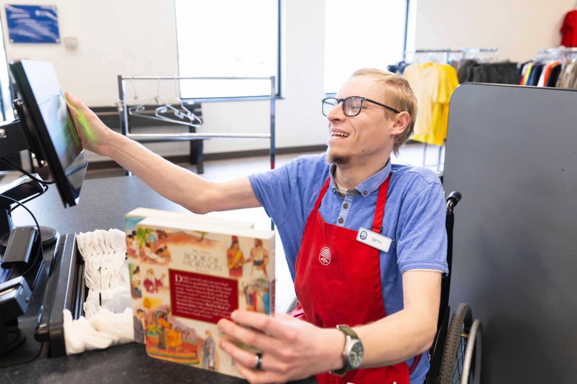 thrift store employee smiles as he works the register as a cashier at Deseret Industries